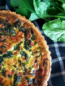 Baked spinach quiche on a dark table cloth.